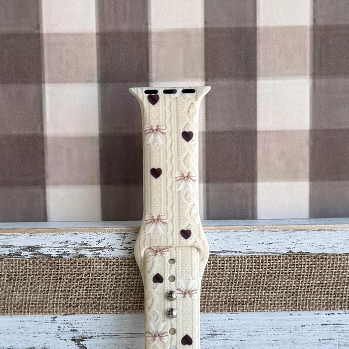 Sweater Weather Sweetheart Apple Watch band shown worn on the wrist with the cream knit, bows, and hearts print visible in daily wear context.