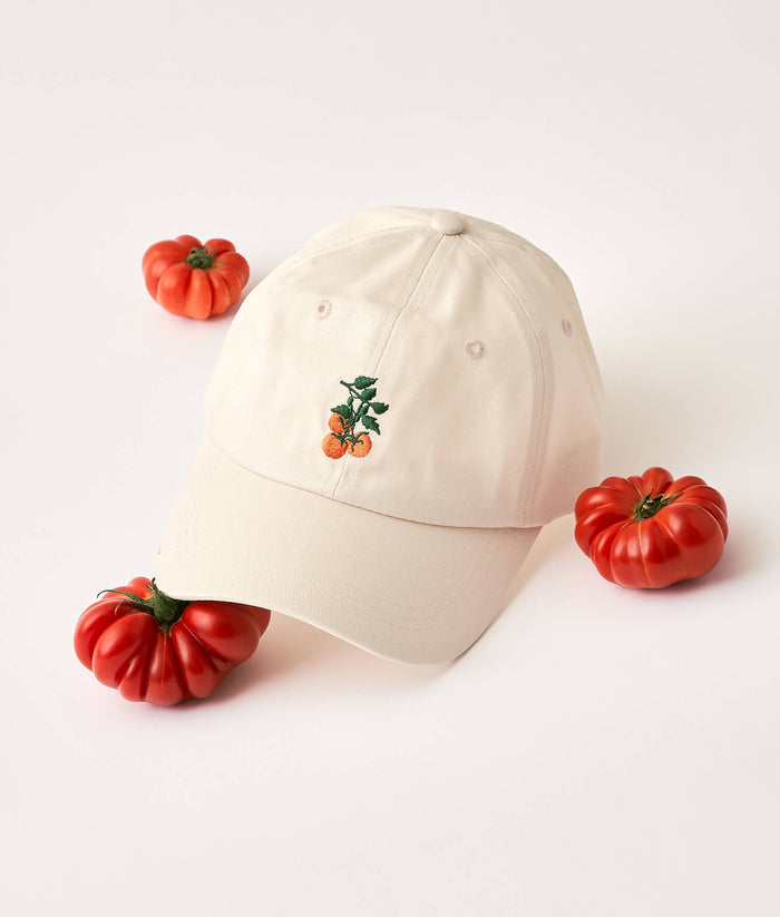 Beige cap with tomato design surrounded by small red tomatoes on a light background