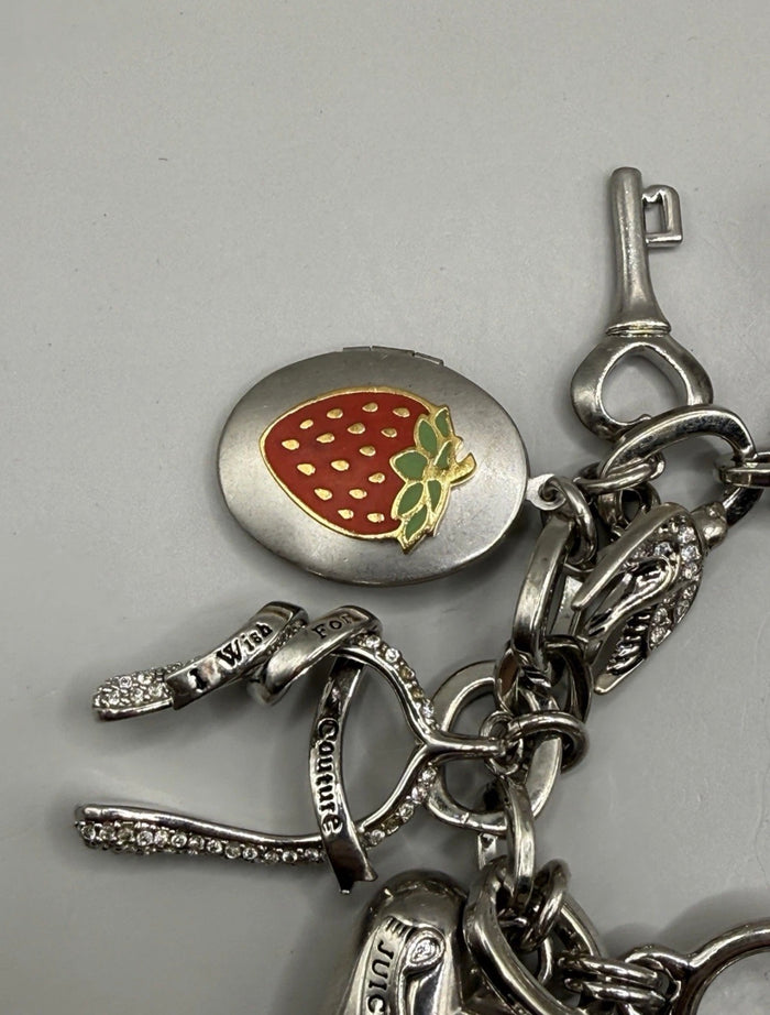 A silver-tone charm bracelet featuring a strawberry-shaped oval pendant, a key-shaped charm, and several small dangling charms, photographed on a plain light gray background.