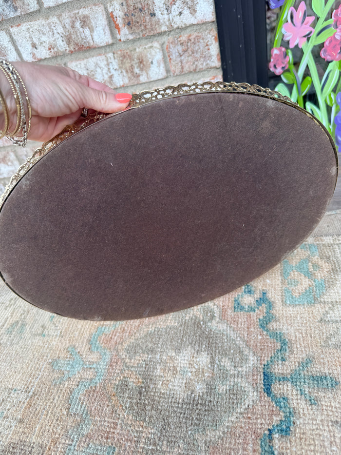 Round brown object with gold trim held by a hand on a patterned rug.