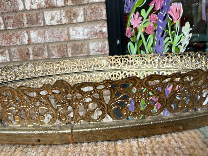 Decorative gold metal frame with floral design against a brick wall.