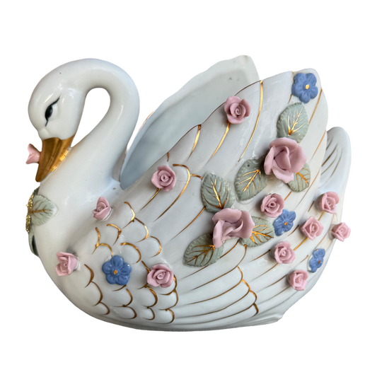 A decorative ceramic swan figurine with a glossy white body, gold-painted lines, and raised pink, blue, and green floral details, shown on a plain white background.